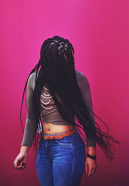 Shot of a young woman with braids posing against a pink background